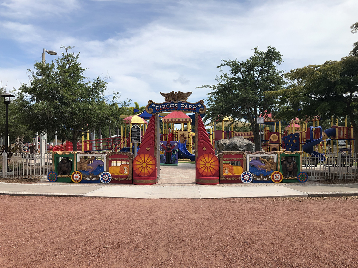 Circus Park Playground at Payne Park. Entrance with circus animals and theme. Sunny day with clouds above. Trail below