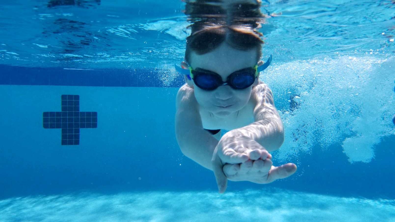 Little boy with goggles on is stream line swimming under water